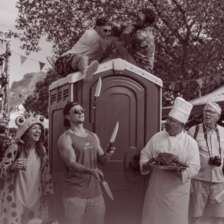 Festival-goers standing by portable toilets at an outdoor music festival.